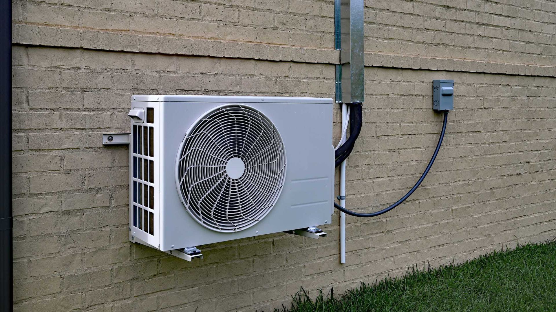 A white air conditioner is mounted on the side of a brick building.