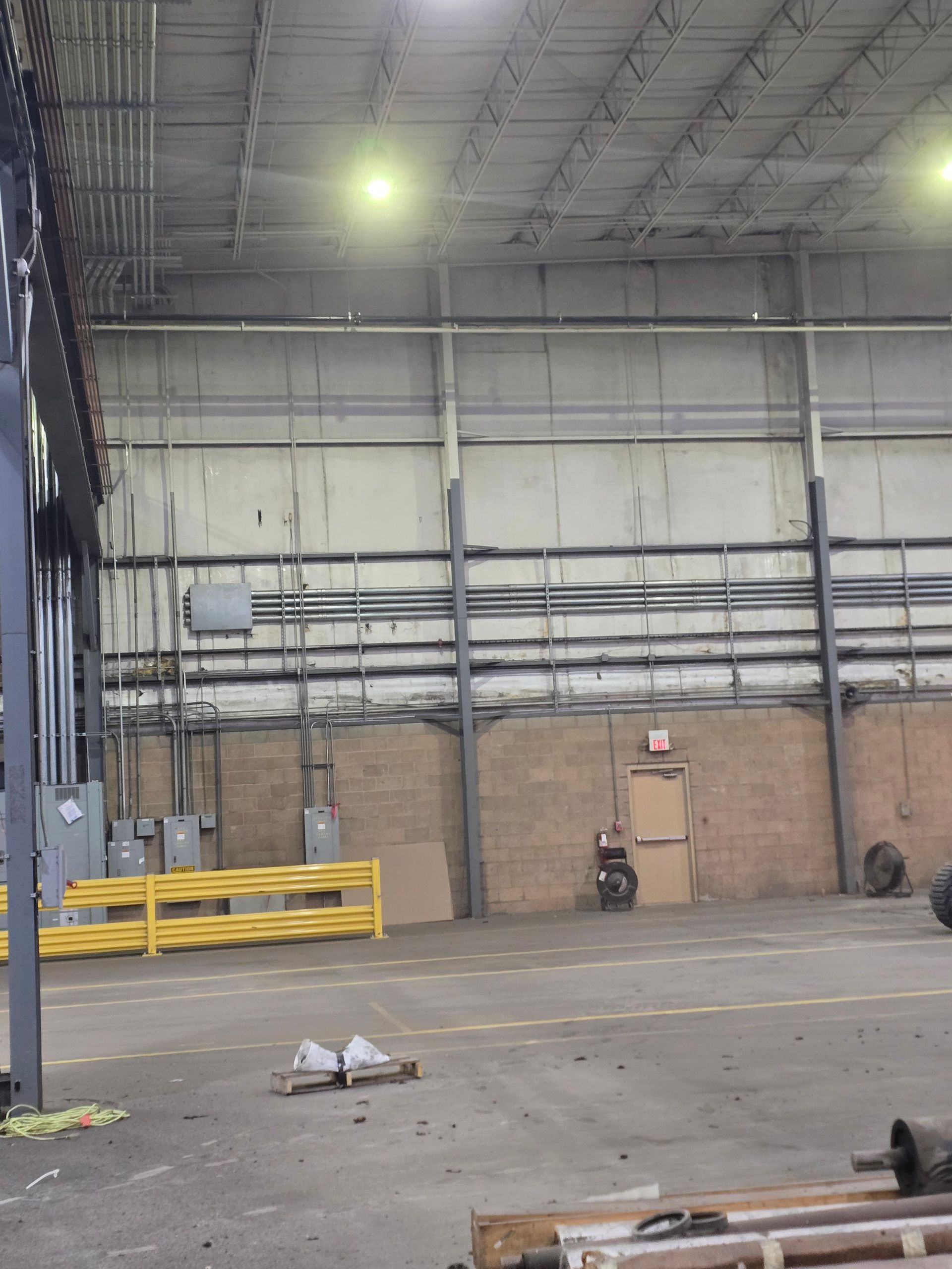 Empty industrial warehouse with concrete floor, metal beams, and utility piping on walls.