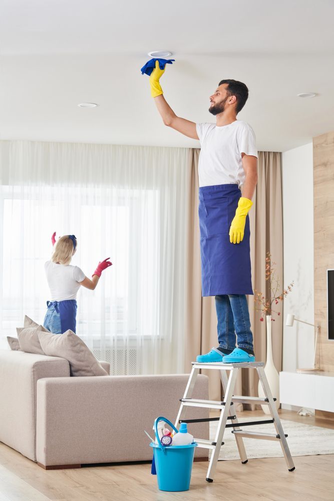 Two people cleaning a room. One on a ladder wiping the ceiling, the other reaching for the ceiling.