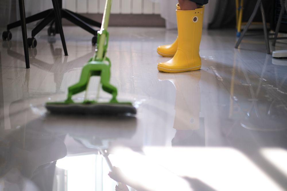 Person wearing yellow boots mopping a shiny floor with a green mop.