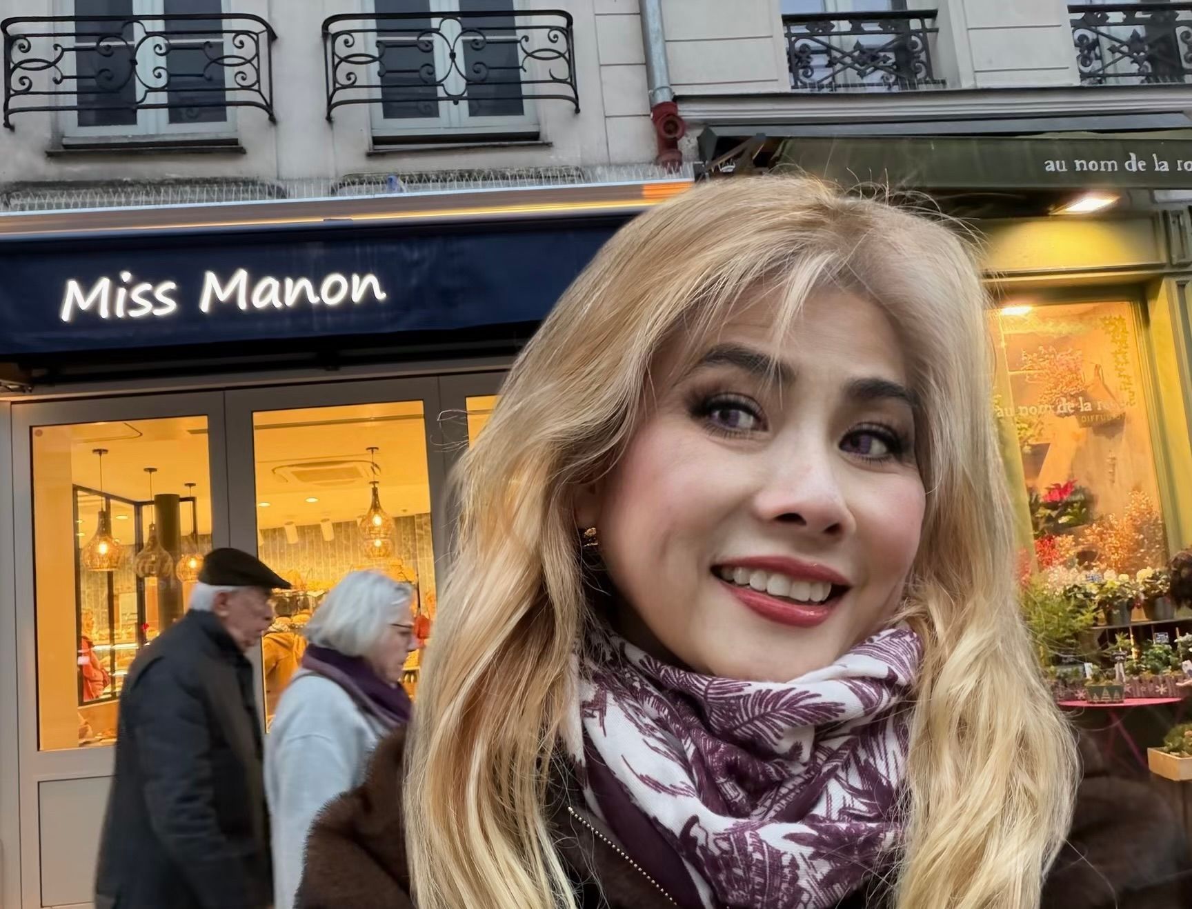 Woman with blonde hair smiles in front of a storefront with 