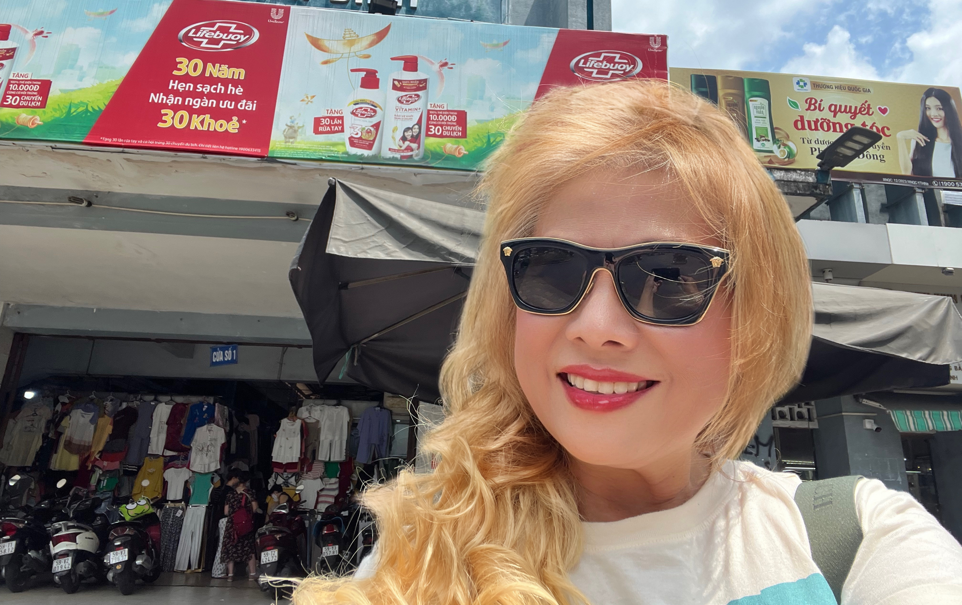 Woman in sunglasses smiles in front of a storefront; clothing racks and parked motorcycles visible.