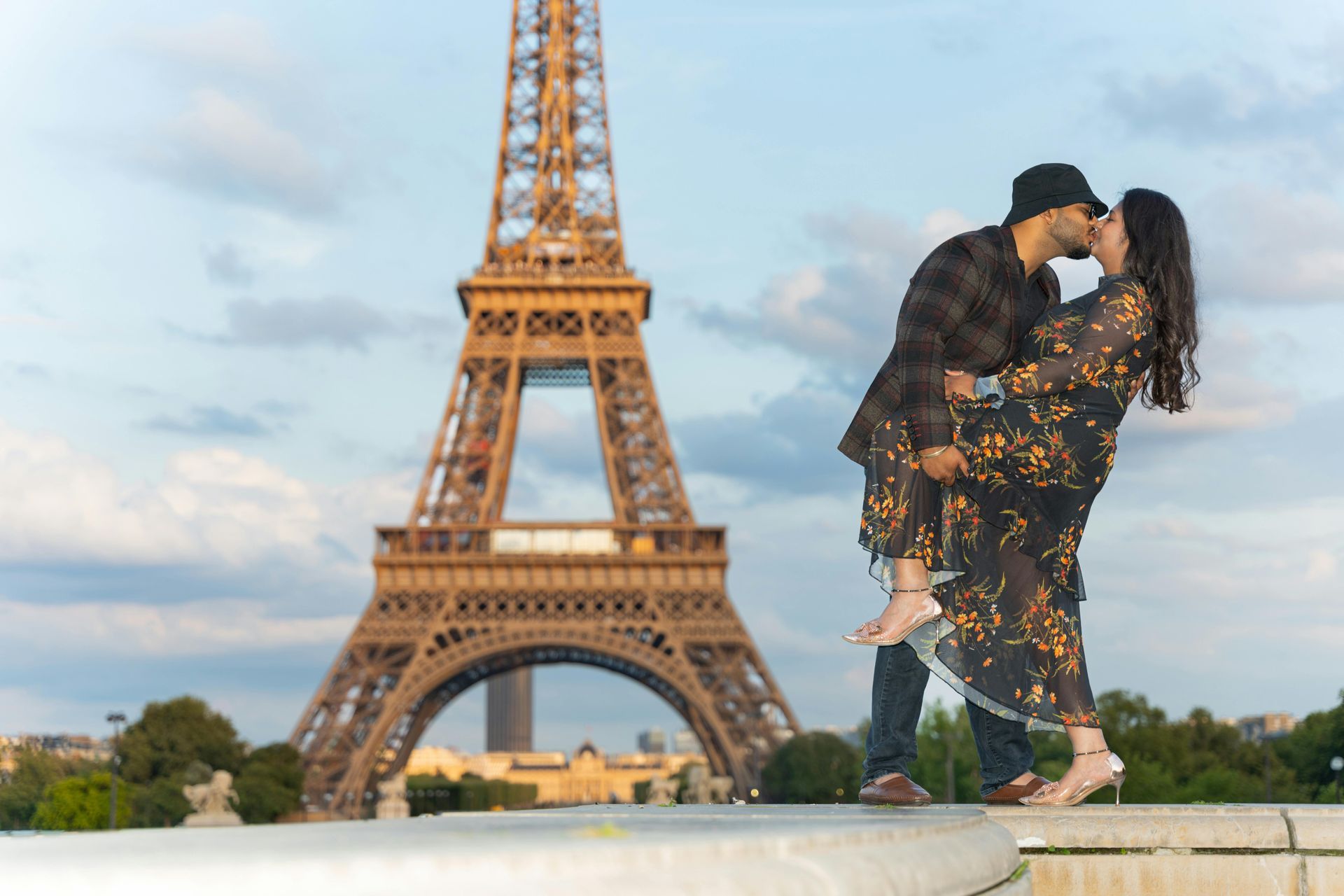 Couple kissing in front of Eiffel Tower; woman dips back, man leans in; sunset.