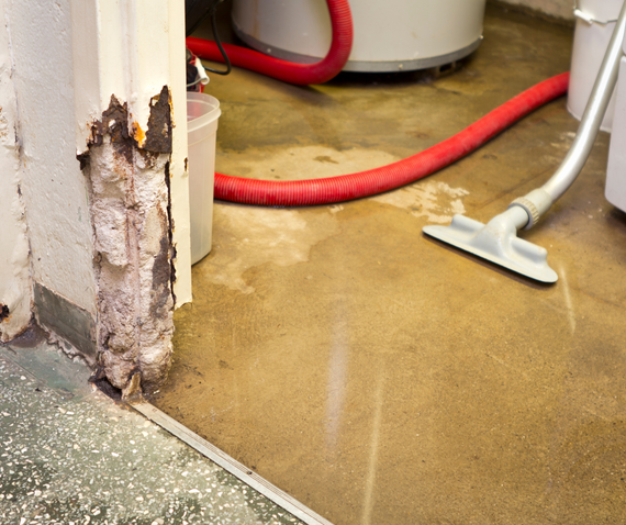 Damaged wall corner with exposed interior. Wet floor, vacuum, water heater in a basement.