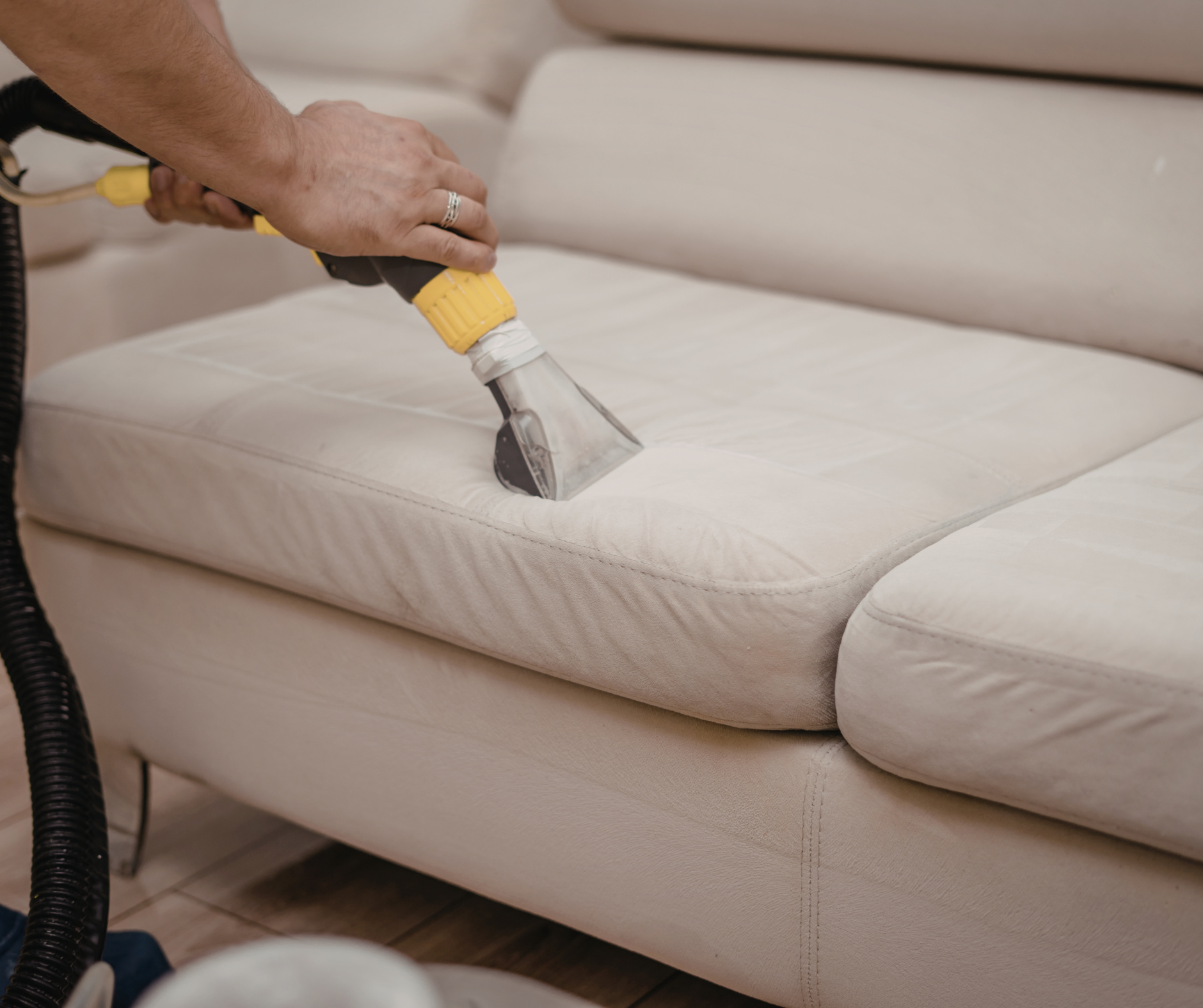 Person cleaning a light-colored sofa with a handheld upholstery cleaner.
