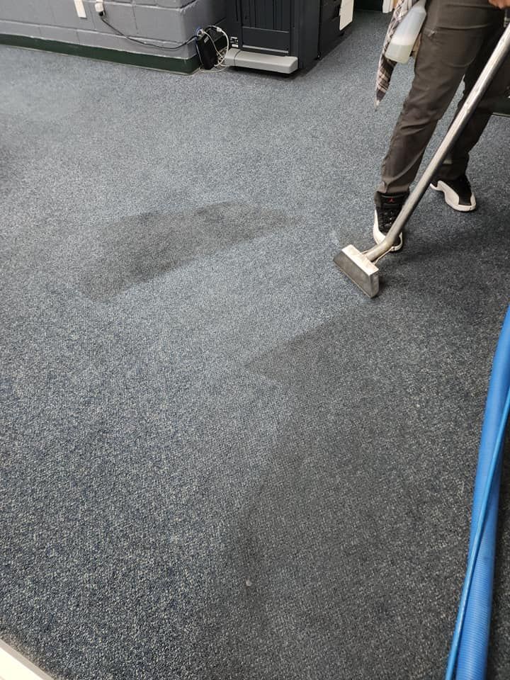 Person steam cleaning a section of a dark blue carpet.