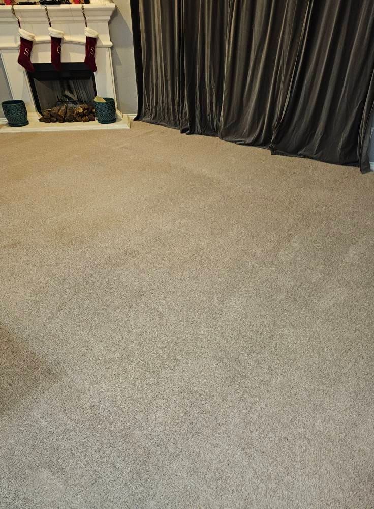 A beige carpeted room with a fireplace and dark curtains.