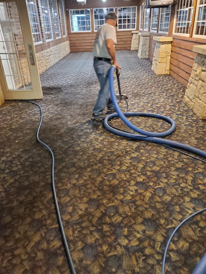 Person cleaning carpet with a machine inside a building with stone walls and large windows.