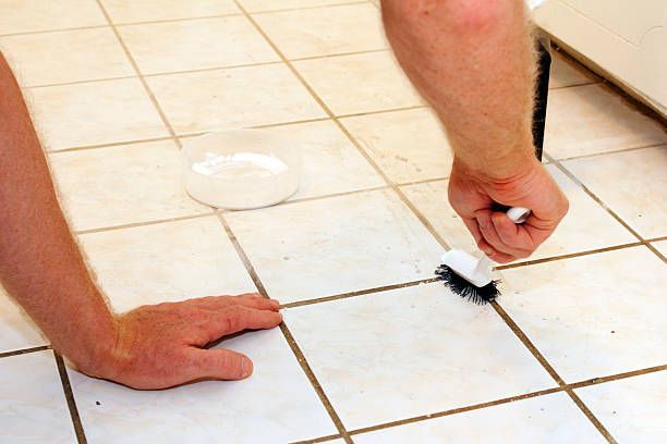 Person scrubbing tile grout with a brush on a tiled floor.