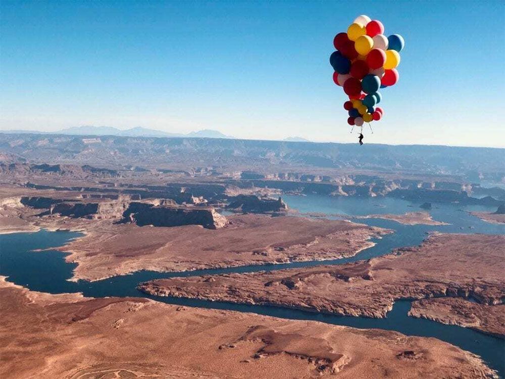A bunch of balloons are floating in the air over a river