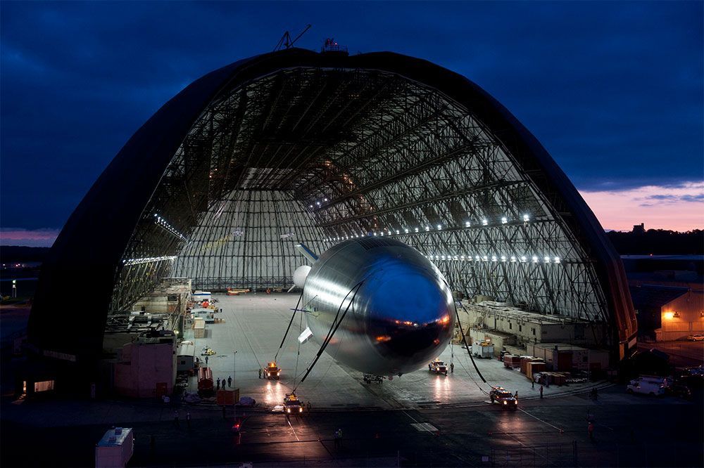 A large airplane is sitting inside of a large hangar at night.