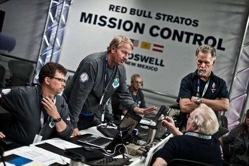 A group of men standing in front of a red bull stratos mission control sign