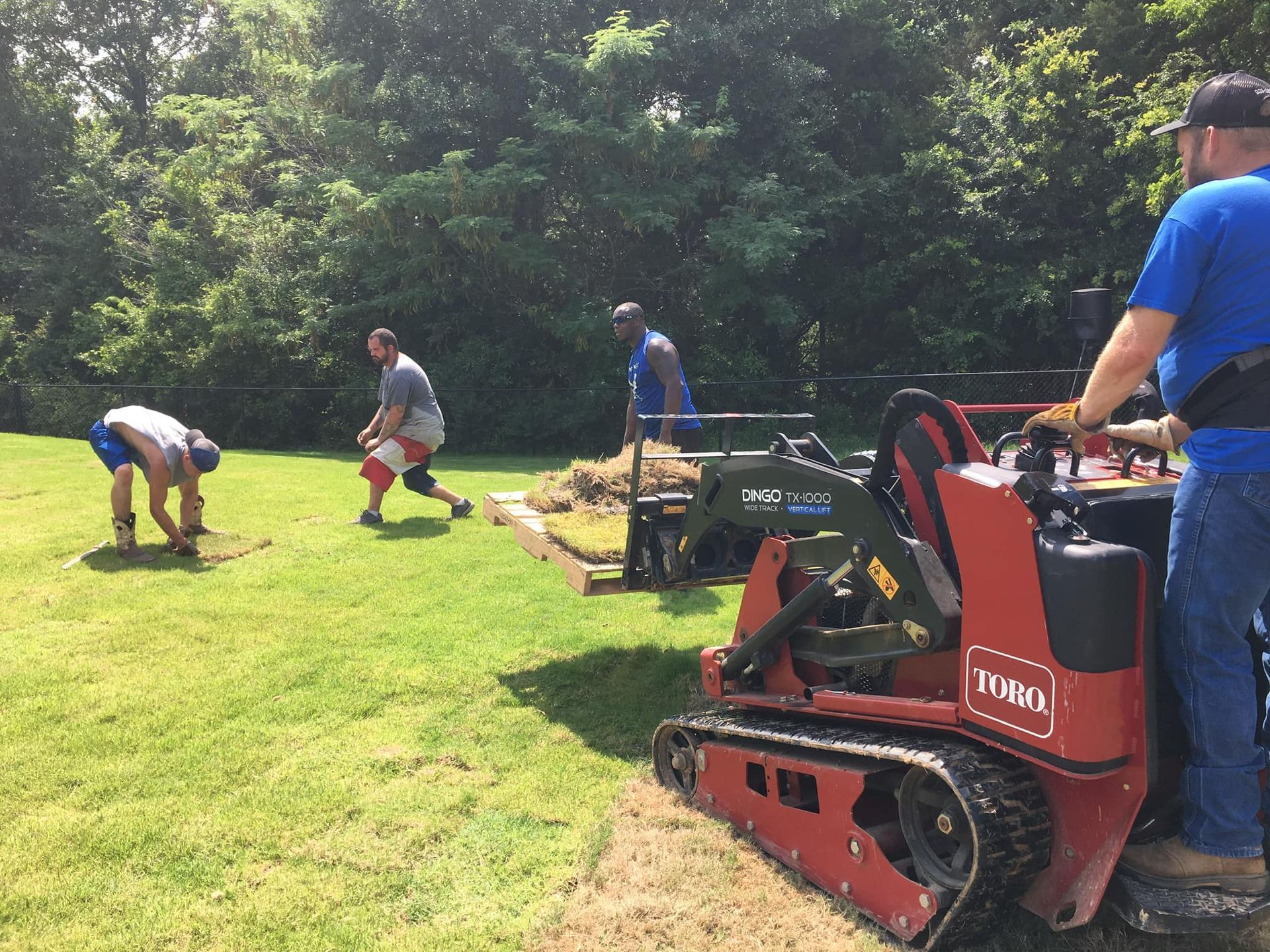 Workers operating machinery on a grassy lawn, likely for landscaping or construction.
