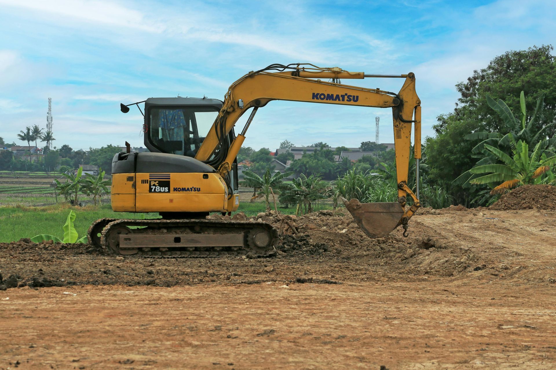 A yellow Komatsu excavator parked on a dirt construction site against a cloudy blue sky.