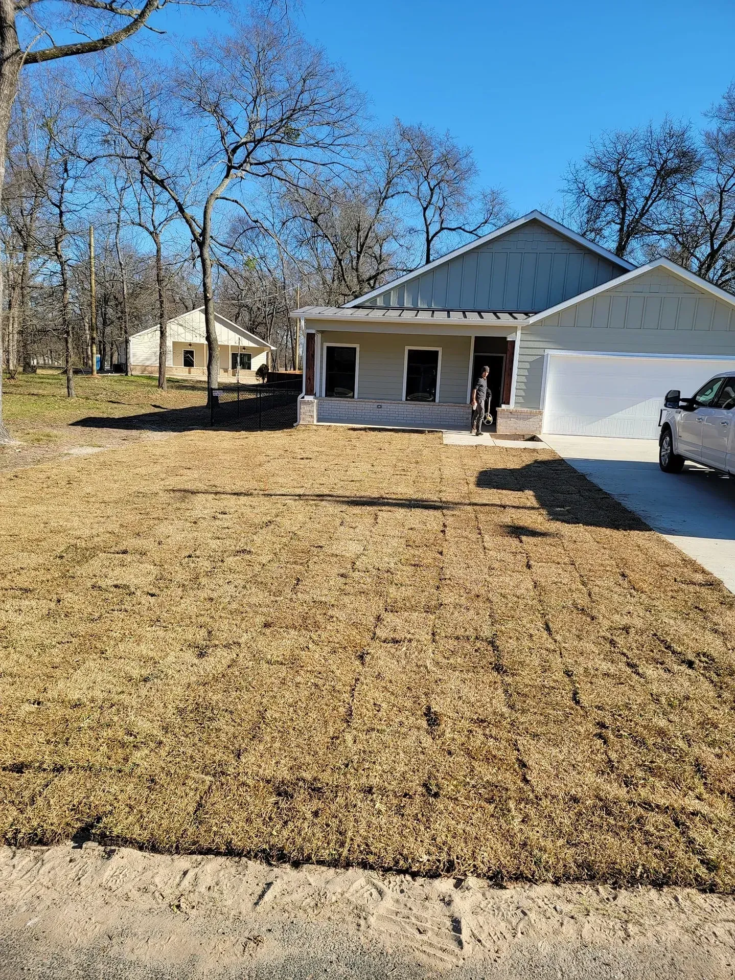 A new house with brown yard. Trees in the background, blue sky, truck parked in the driveway.