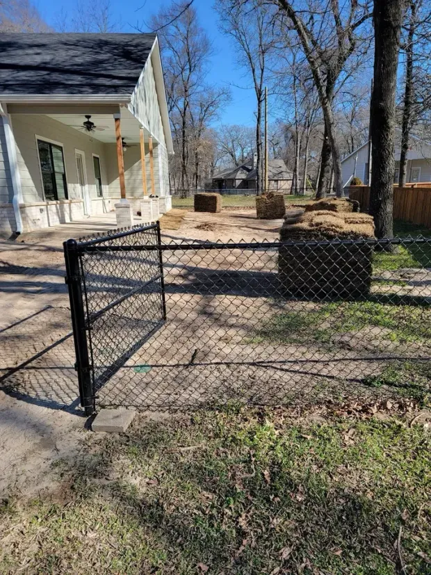 Black chain-link fence with hay bales, yard area near a house.
