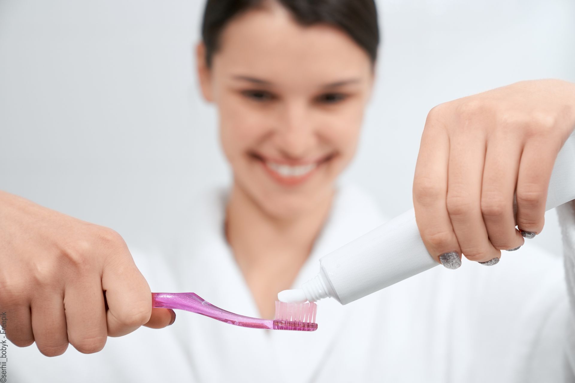 Uma mulher está a colocar pasta de dente numa escova de dentes.