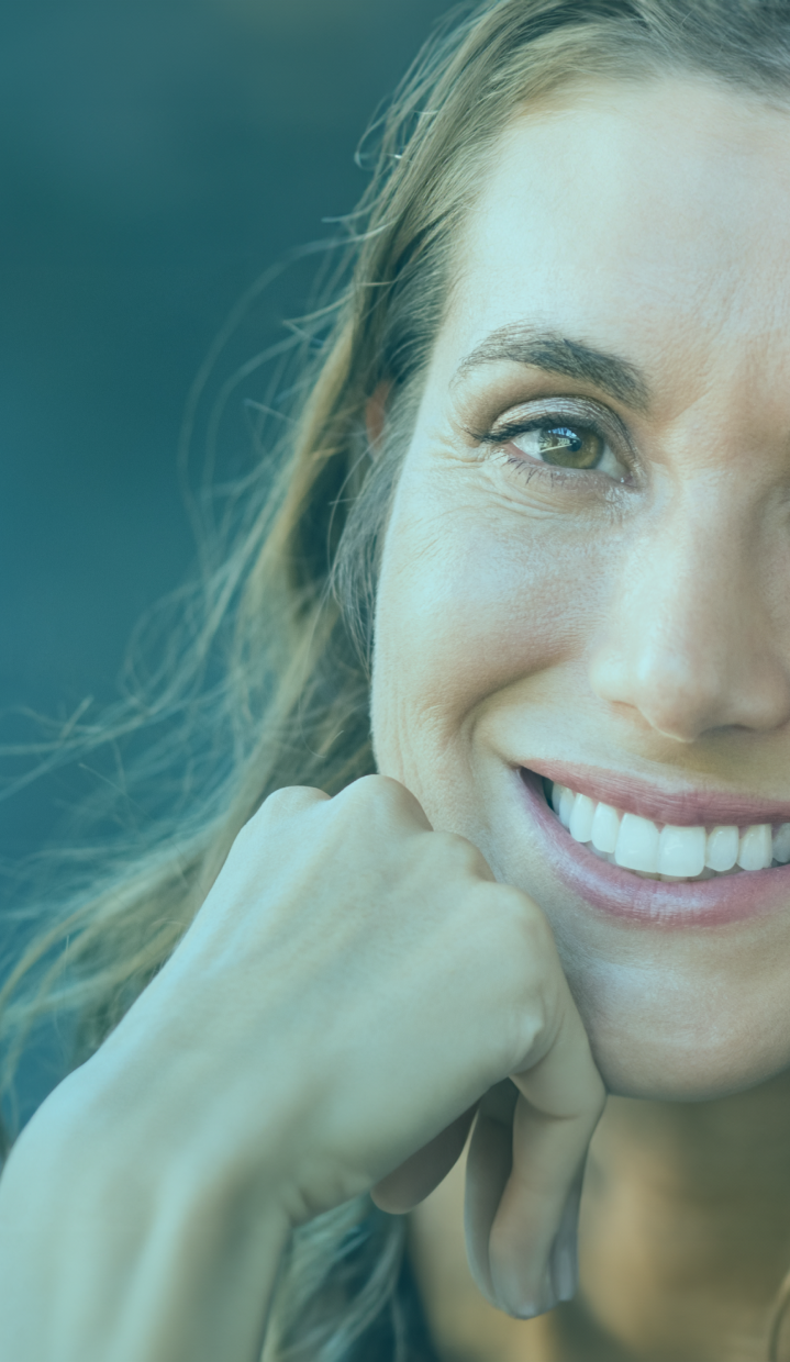 Portrait of a smiling woman with short blonde hair, displaying a confident, healthy smile with shiny teeth, the result of successful dental implants. She is wearing a light pink blouse and the background is dark blue, highlighting her happy, rejuvenated expression.
