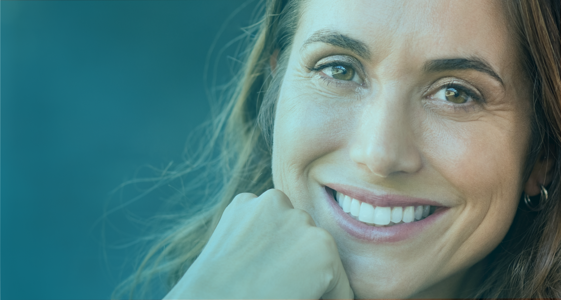 Portrait of a smiling woman with short blonde hair, displaying a confident, healthy smile with shiny teeth, the result of successful dental implants. She is wearing a light pink blouse and the background is dark blue, highlighting her happy, rejuvenated expression.
