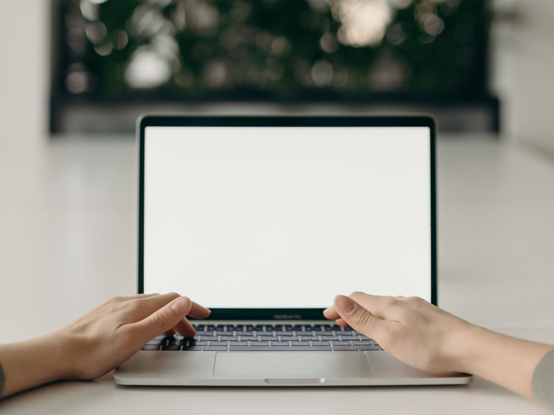 A person is typing on a laptop computer with a white screen.