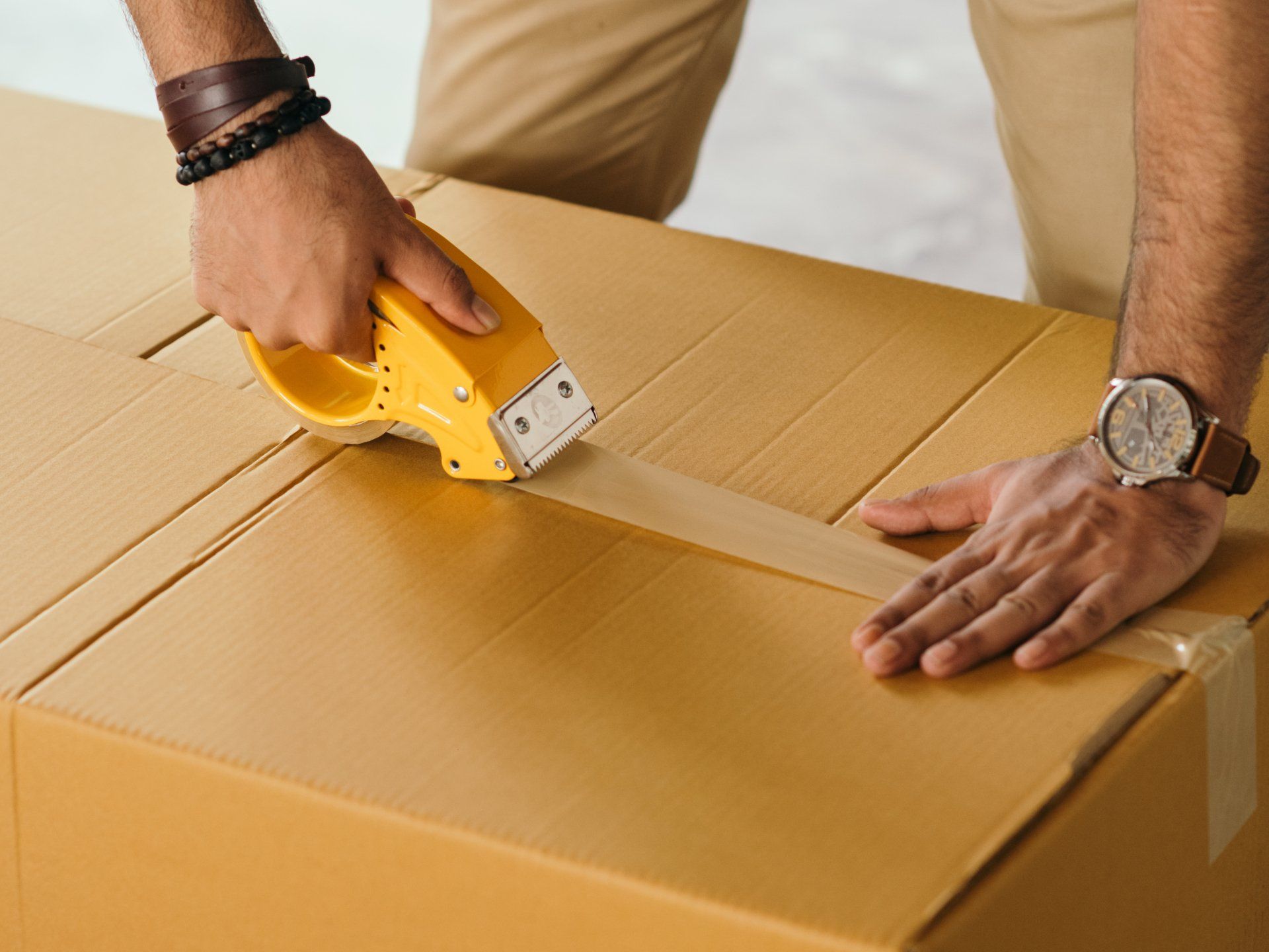 A man is taping a cardboard box with tape.