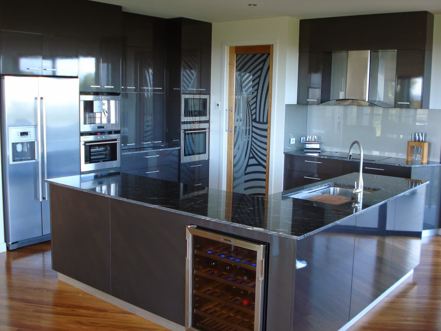 A Modern Kitchen With Dark Finishes and Wooden Floor — Grant Wannan Plumbing in Wollongbar, NSW