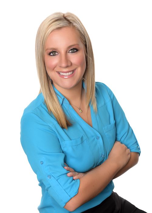 A woman in a blue shirt is smiling with her arms crossed
