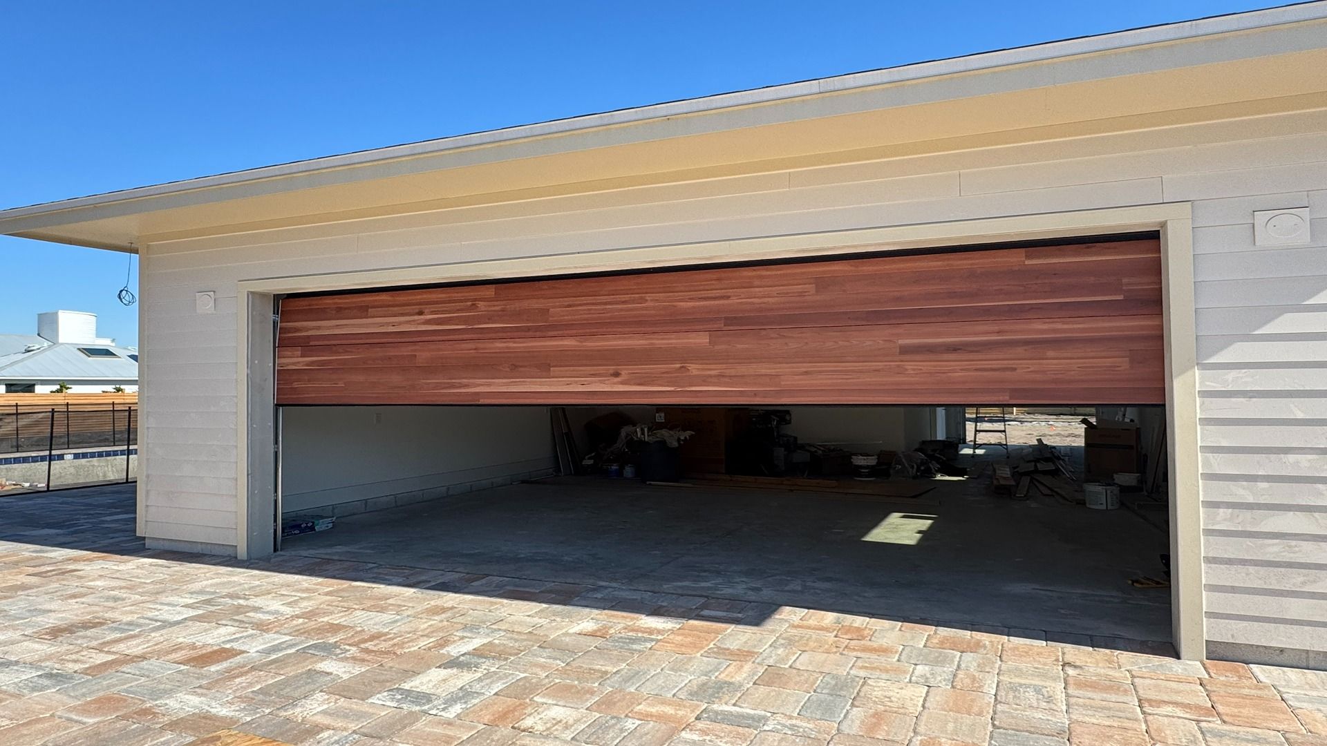 A modern, wide garage featuring a partially raised wooden-slatted sectional door on a sunny day.