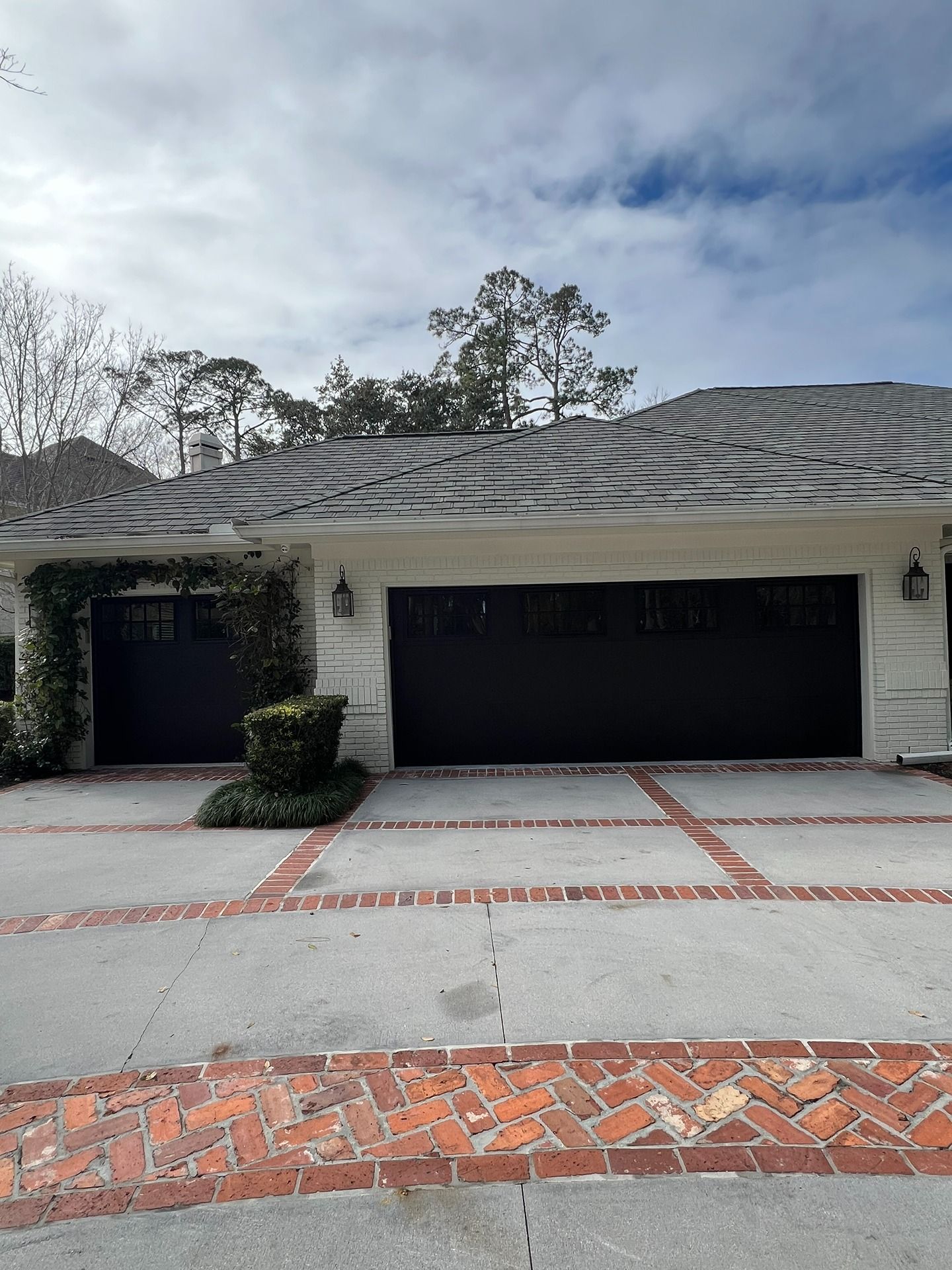 A multi-car garage with black doors and white stucco walls, featuring a concrete driveway with red brick accents.