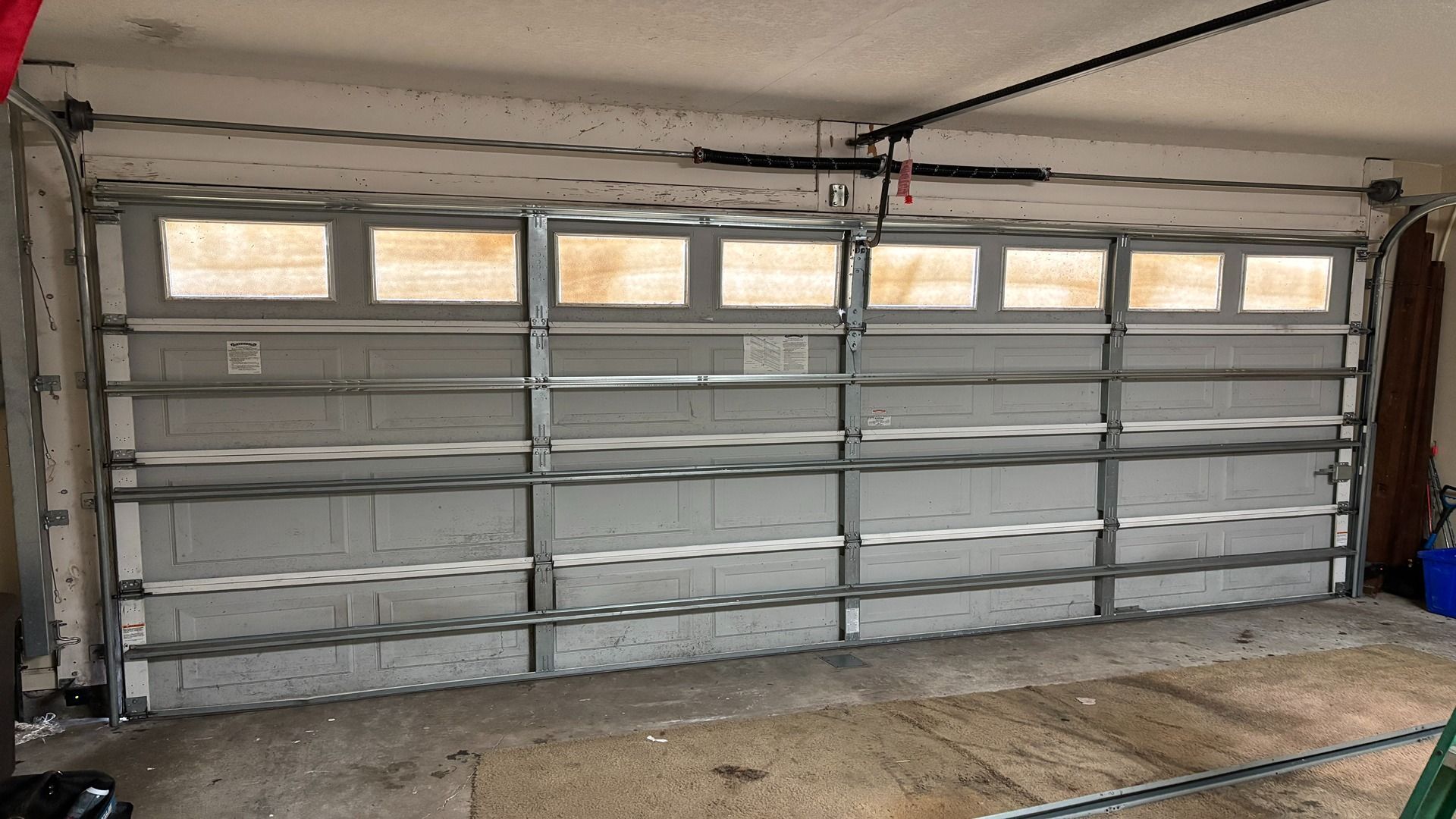 An interior view of a closed, light-gray sectional garage door with a row of rectangular windows at the top.