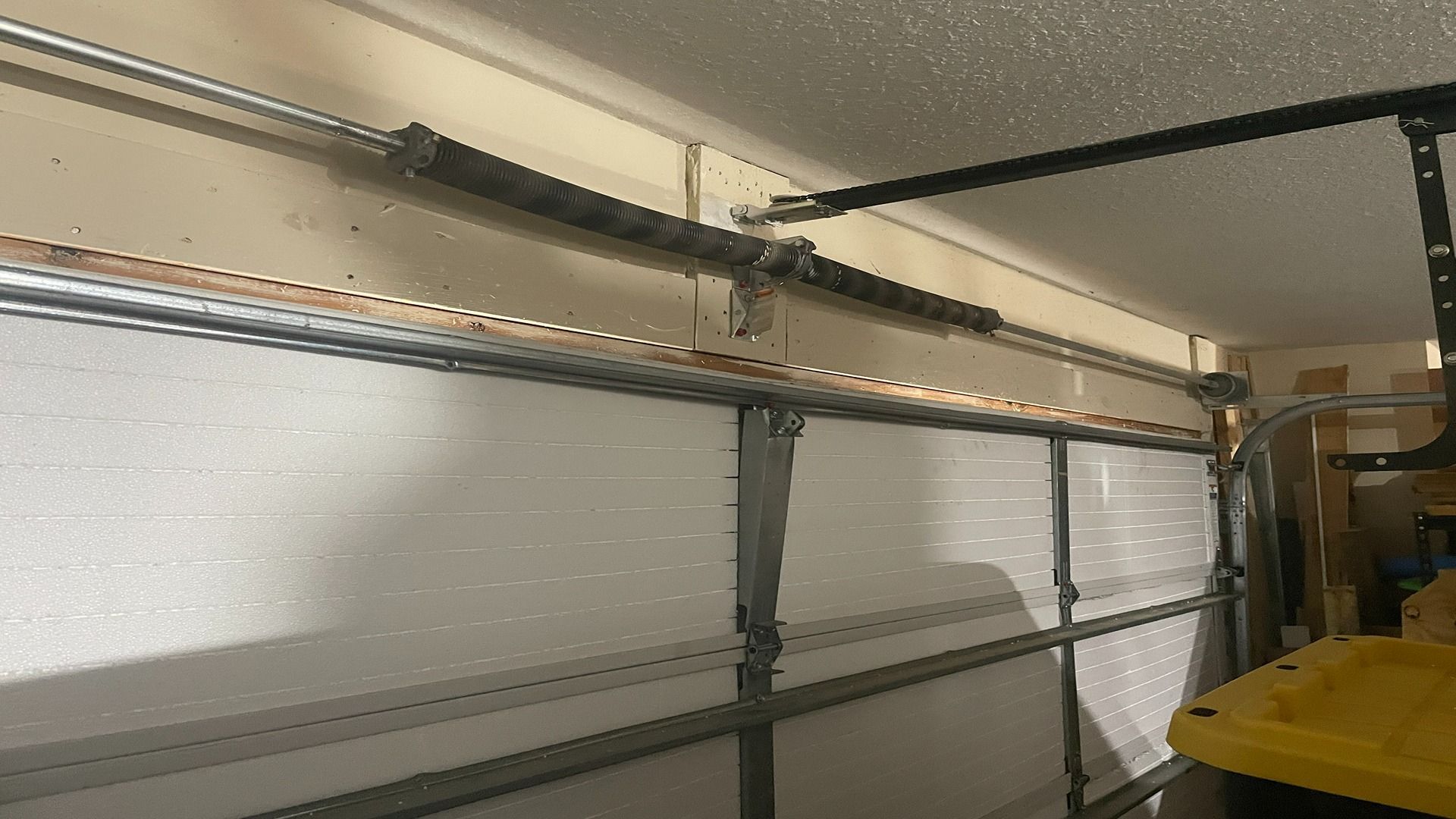 A view of a garage door interior, showing the metal spring assembly mounted horizontally above the top panel.