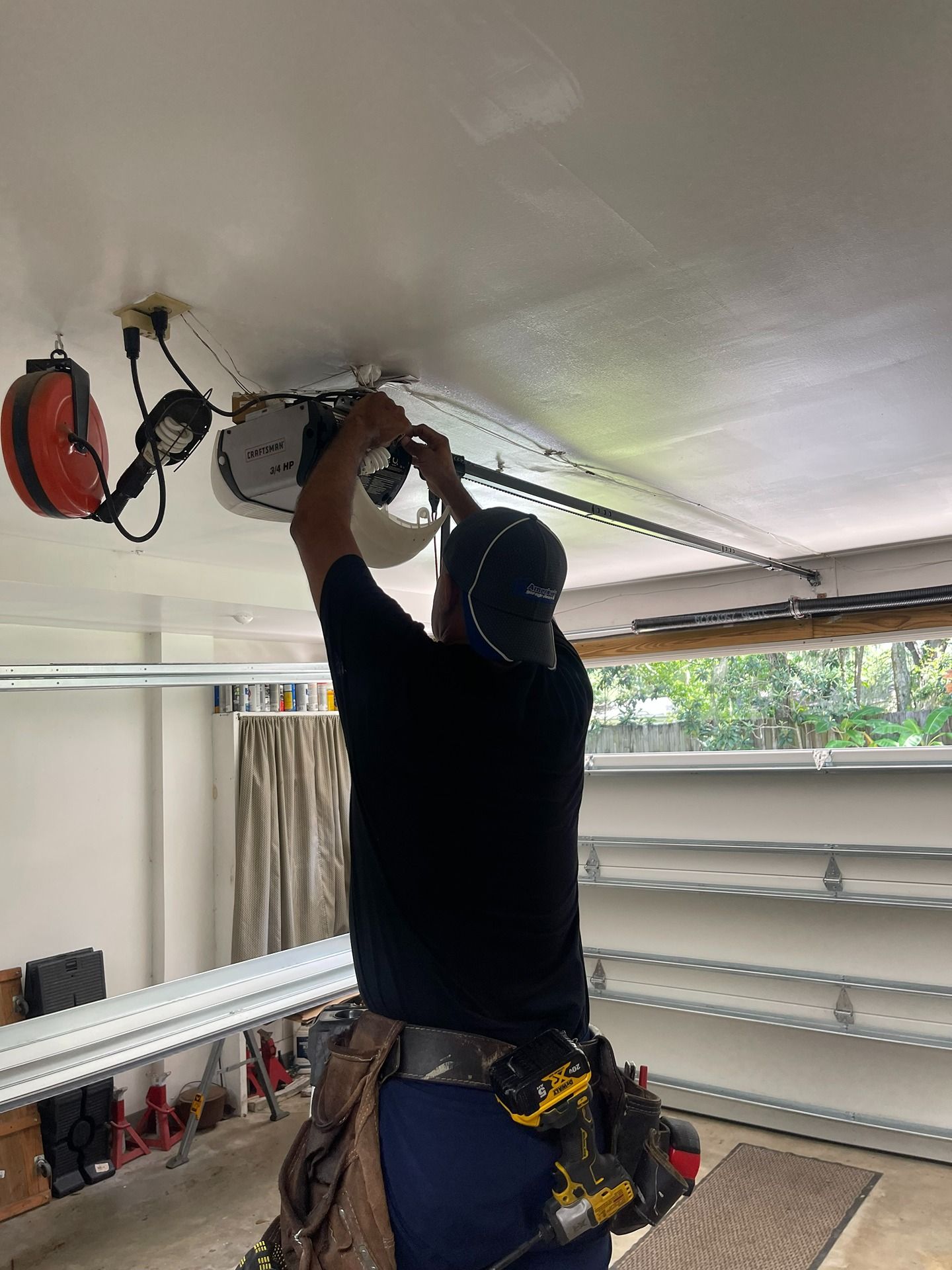 A technician in a black shirt installs a garage door opener motor on a ceiling.