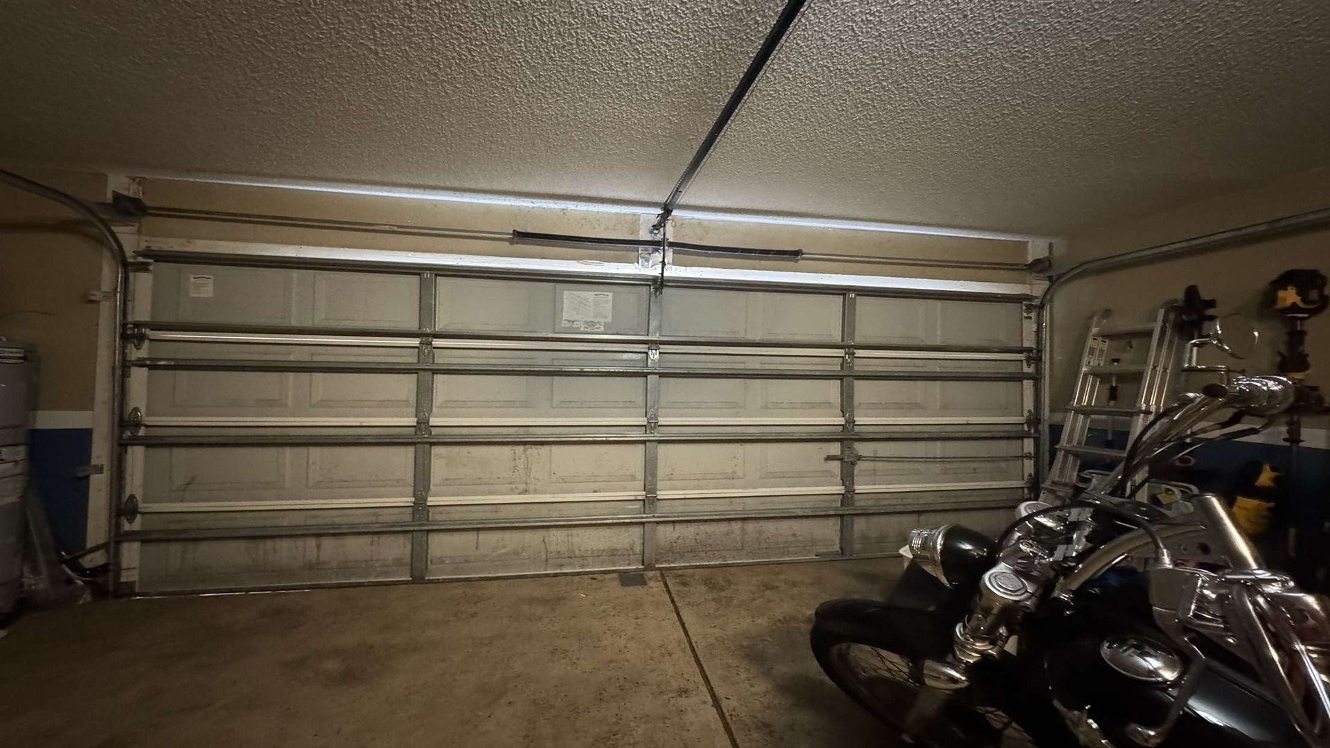 Inside view of a garage with a large metal sectional door and a motorcycle parked in the lower right foreground.