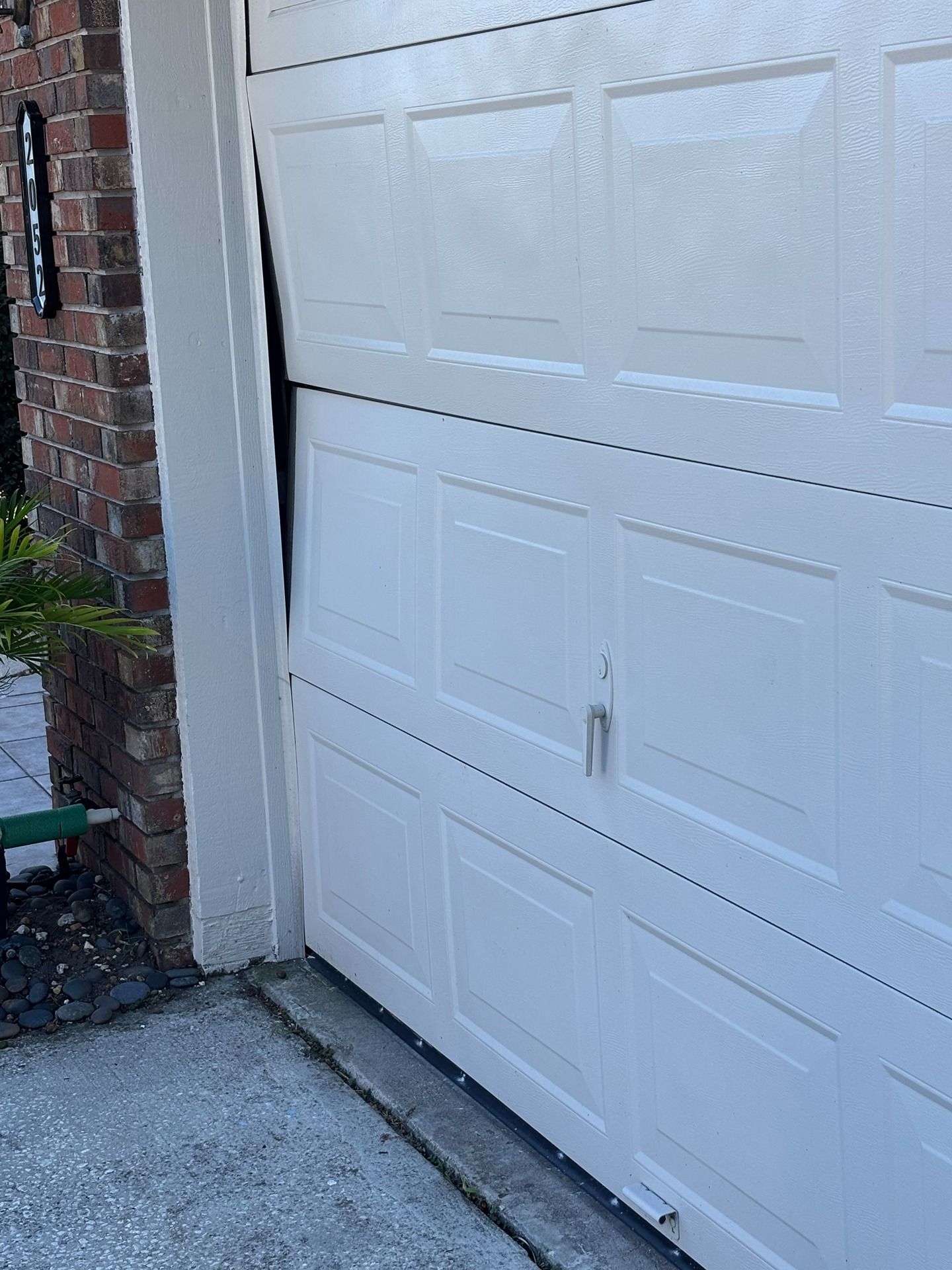 A white garage door is visibly misaligned and pulled away from the frame on the left side.