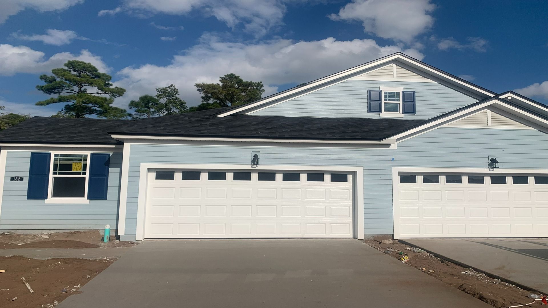 A light blue, single-story house with a three-car garage and dark blue window shutters under a partly cloudy sky.