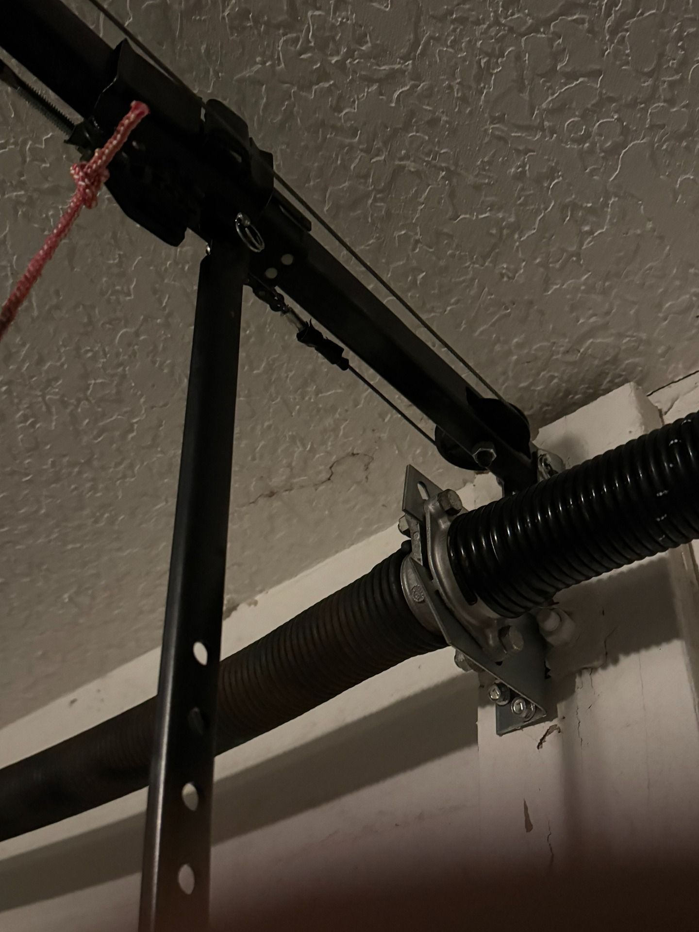 A garage door torsion spring and metal rail system mounted on a wall and ceiling.