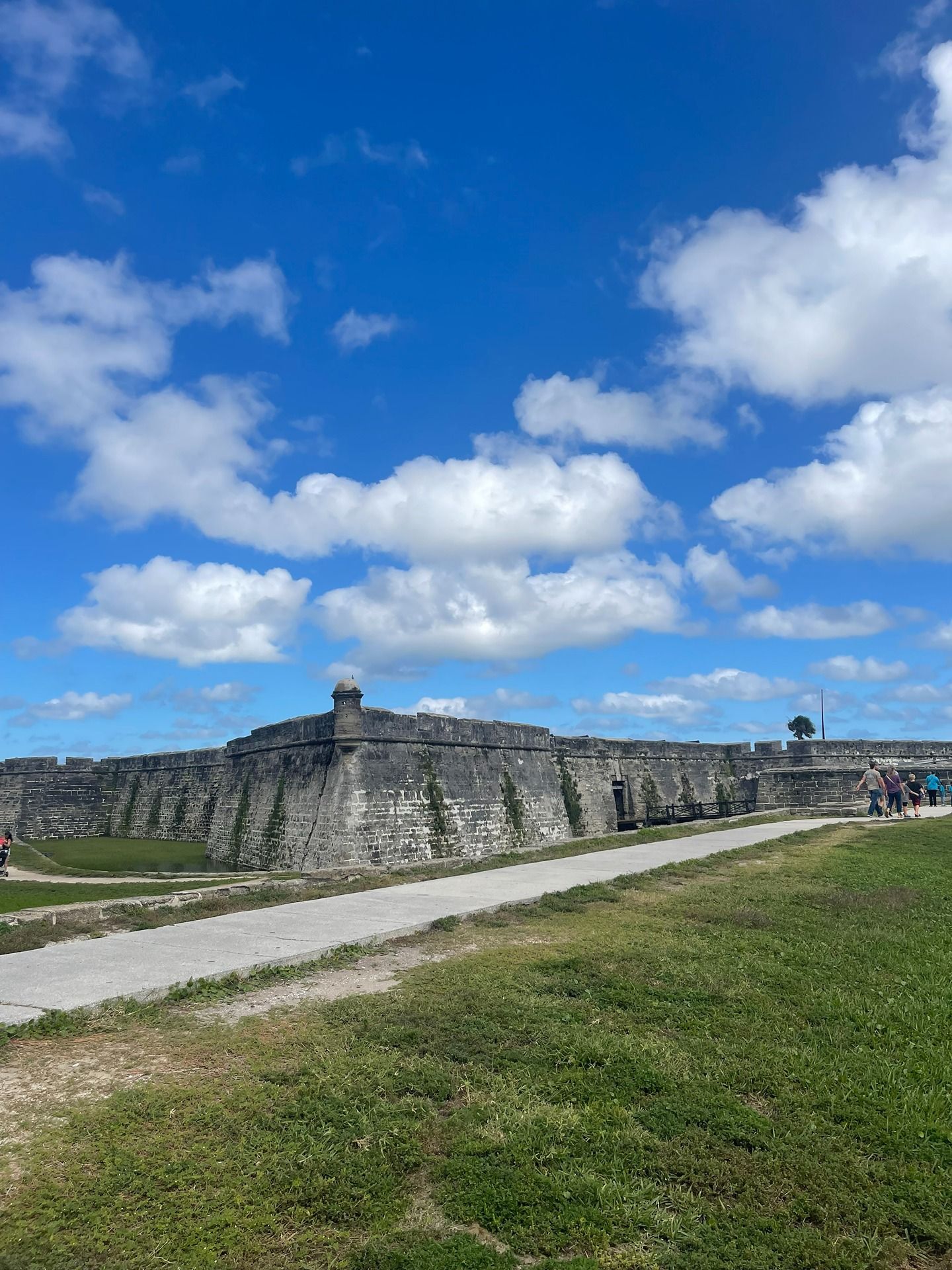The historic stone walls of Castillo de San Marcos under a bright blue, cloudy sky, with a path in the foreground.