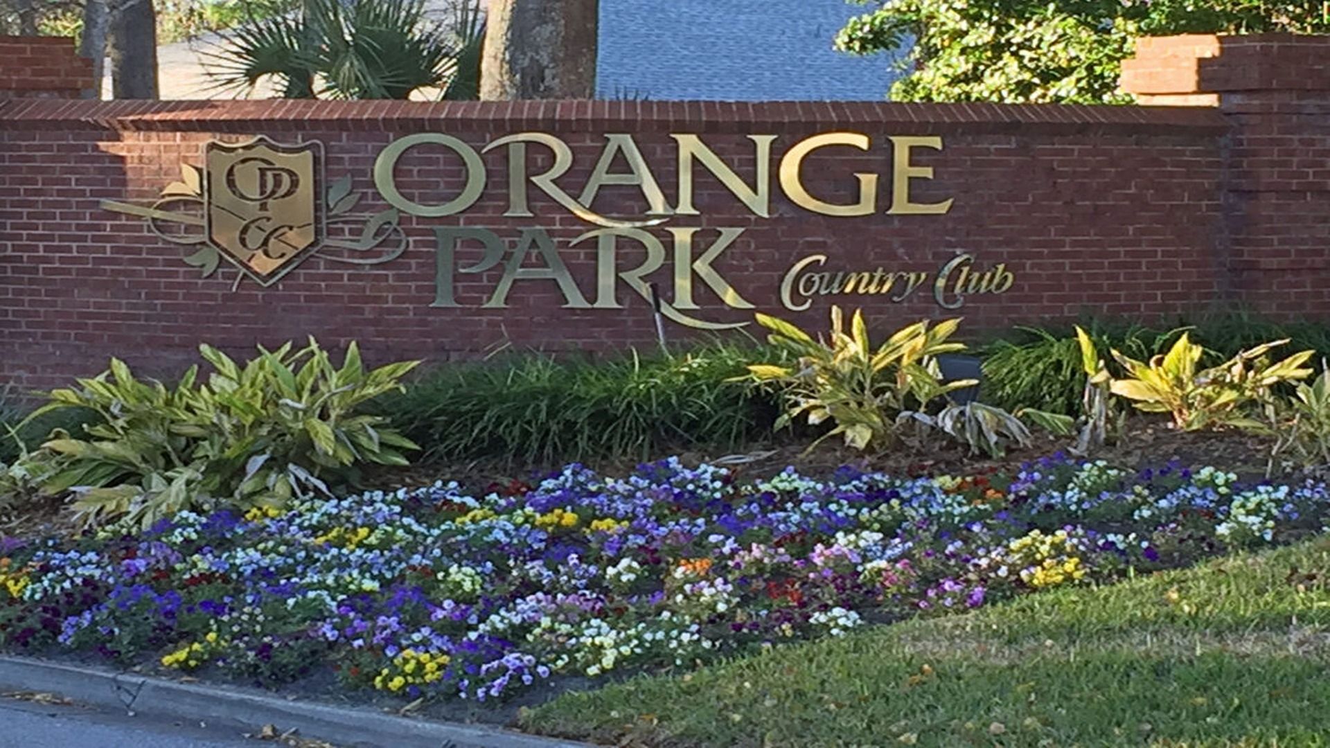 A brick sign for the Orange Park Country Club surrounded by landscaping and a bed of purple and yellow flowers.