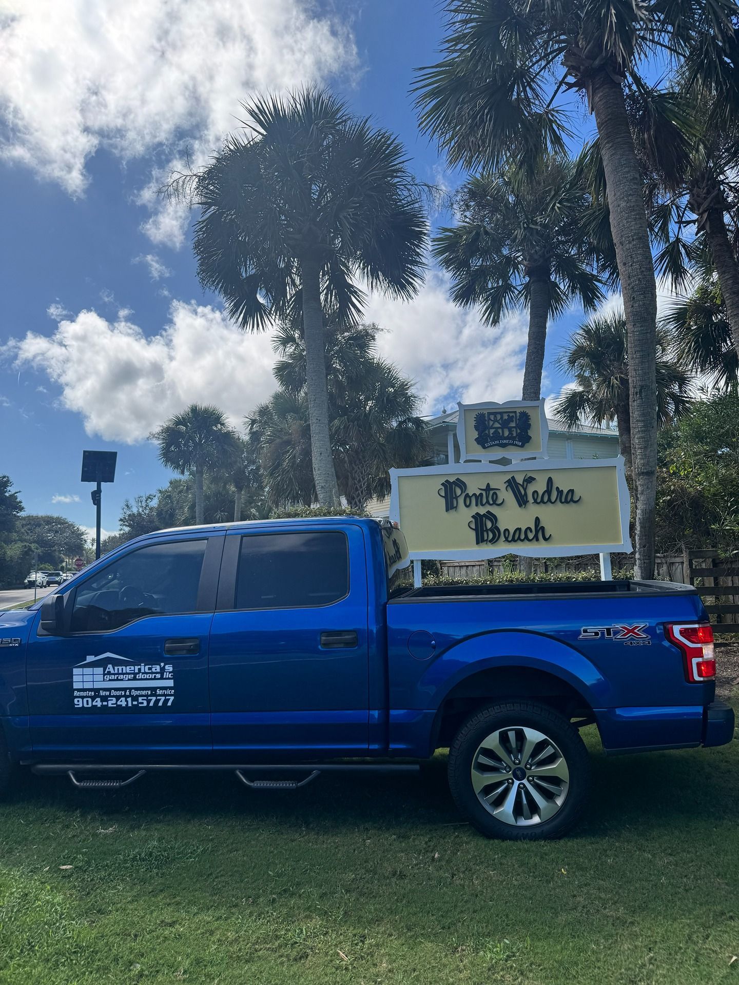 A blue pickup truck parked on grass, carrying a sign that reads 