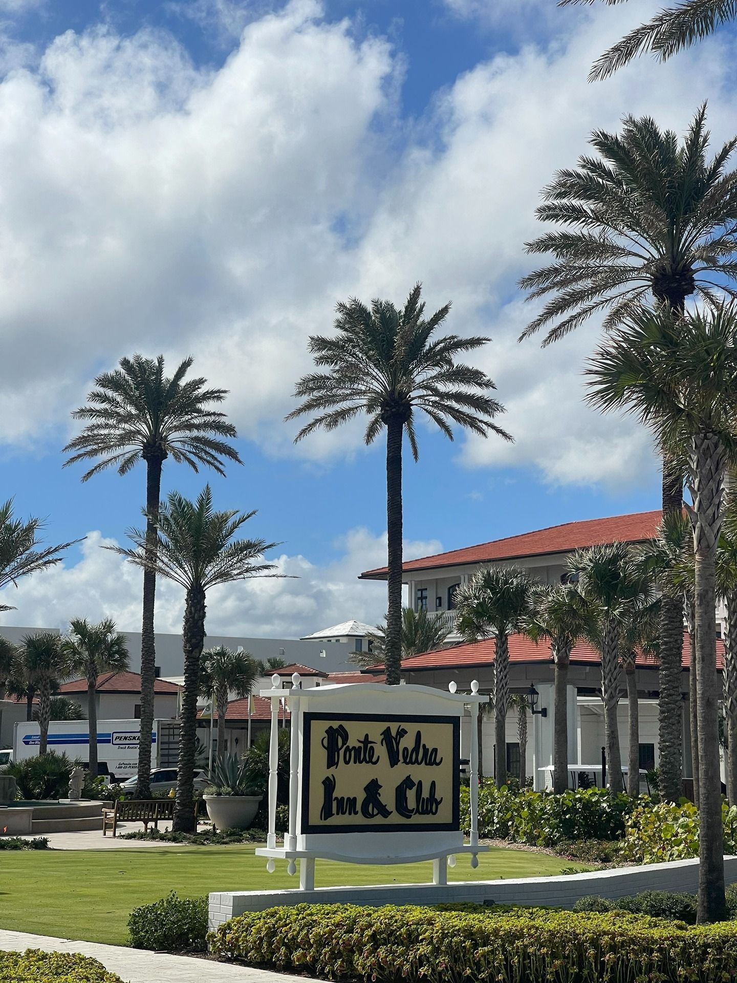 A sign for the Ponte Vedra Inn & Club surrounded by palm trees against a blue sky with white clouds.