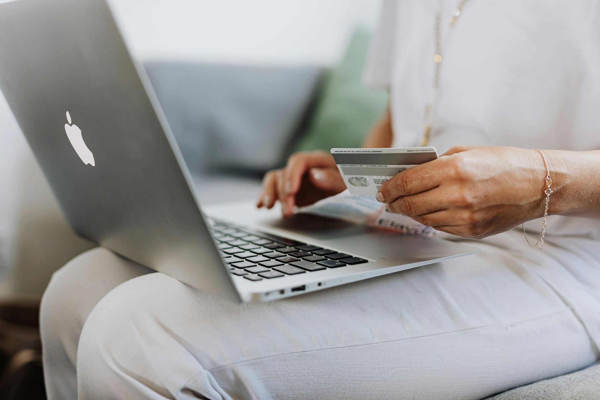 A woman is holding a credit card while using an apple laptop.