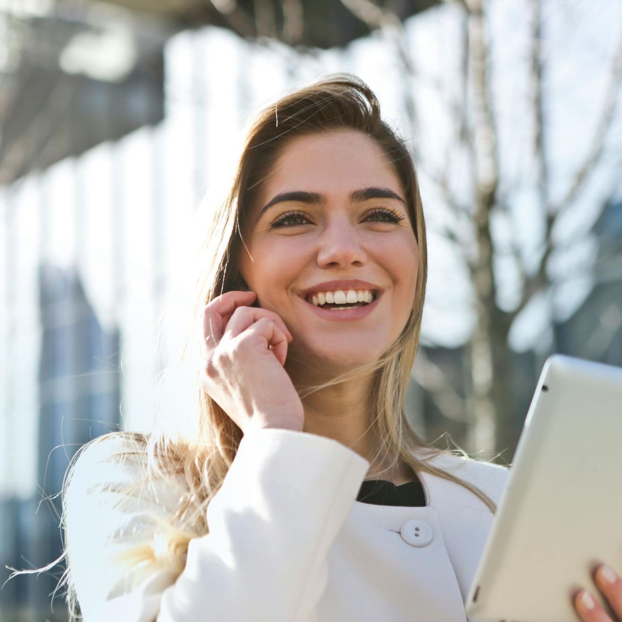 A woman is smiling while holding a tablet and talking on a cell phone