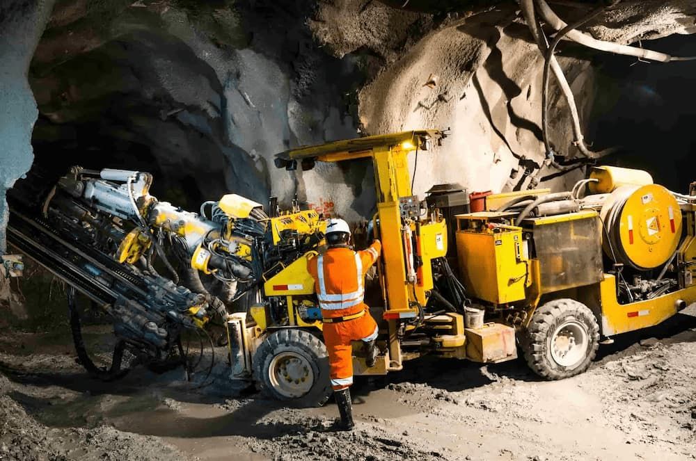 A Man is Standing Next to a Yellow Machine in a Tunnel — Secure Mine Solutions In Ryan, QLD