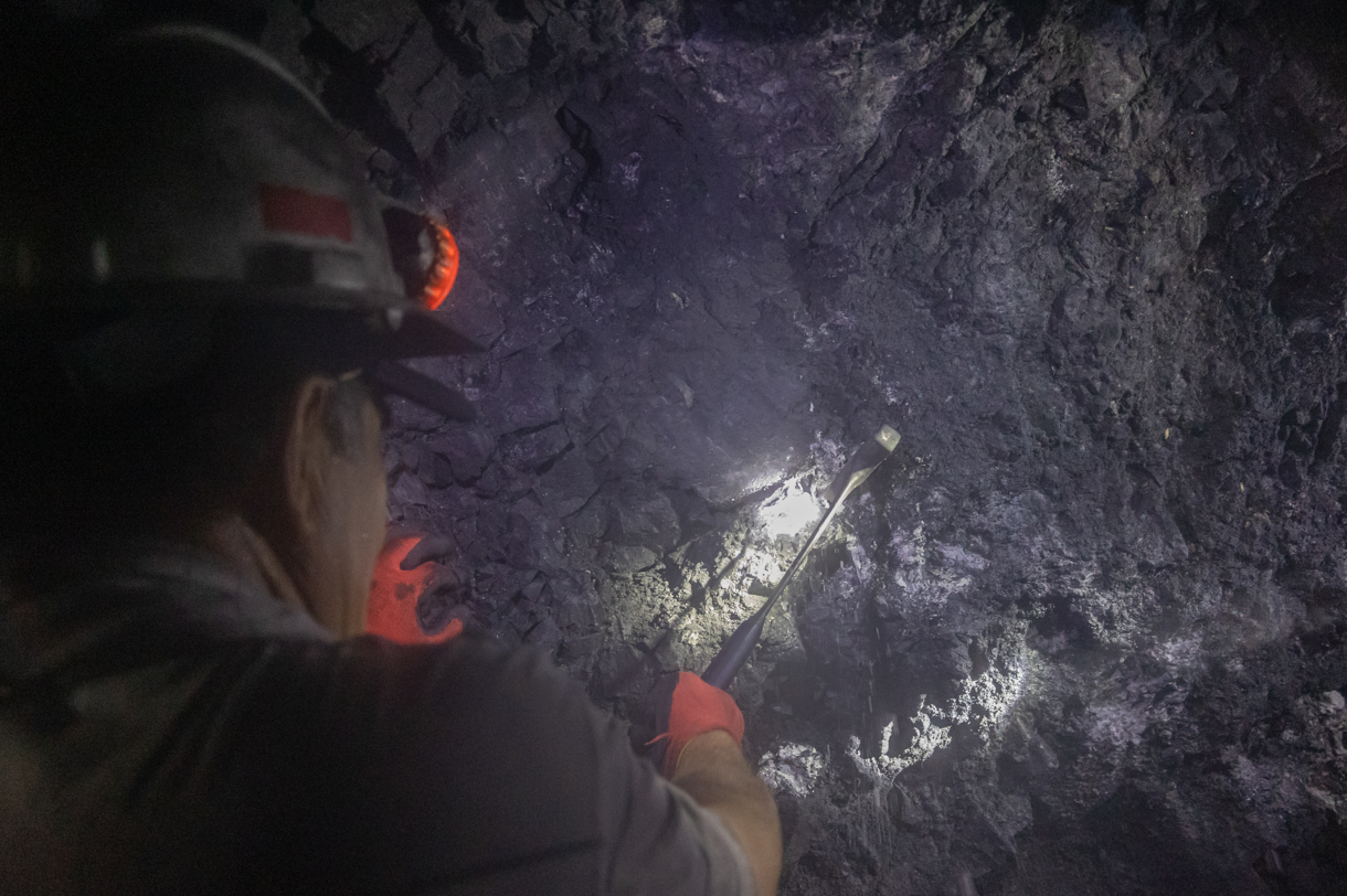 A Man is Working in a Coal Mine With a Flashlight — Secure Mine Solutions In Ryan, QLD