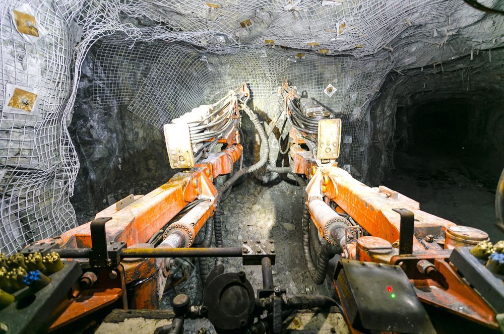 A Man Wearing a Hard Hat and Safety Vest is Digging in a Pile of Coal — Secure Mine Solutions In Ryan, QLD