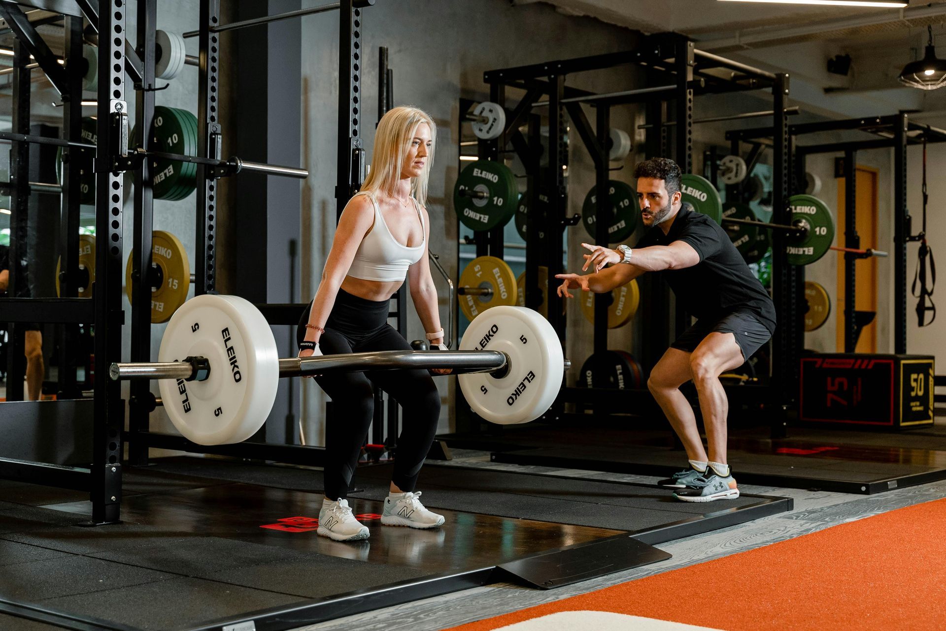 A personal trainer with a woman at the gym helping to perfect her deadlift form