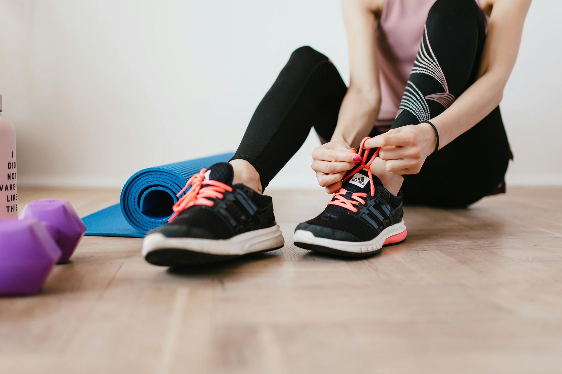 A woman near a fitness mat tying her shoes up
