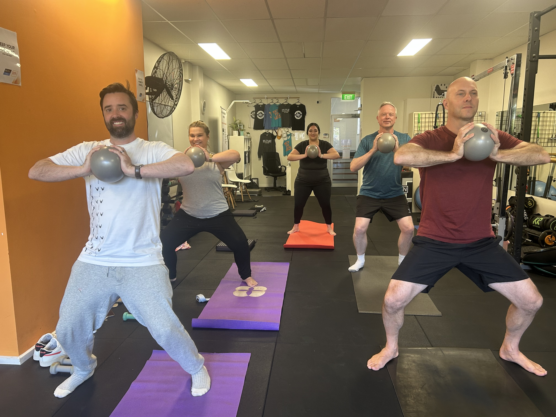 Pilates Class clients holding standing squat pose with Pilates balls in hand