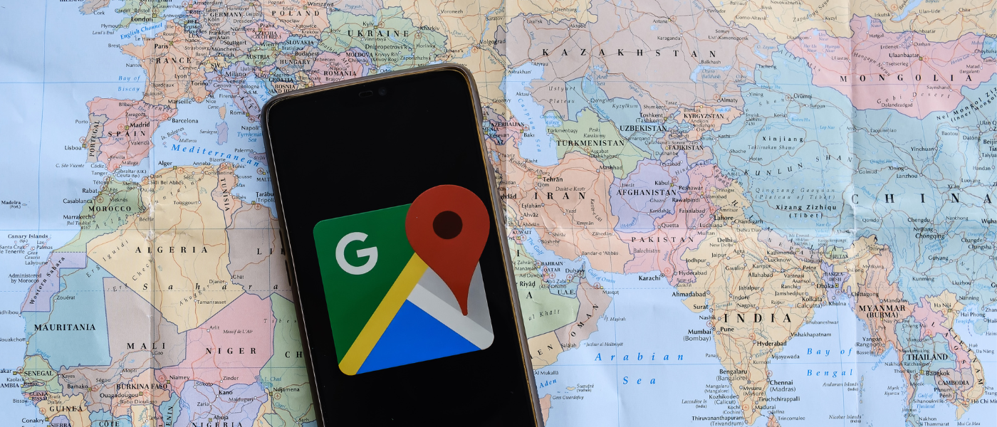 a photo of a smartphone laying on a map with the Google Maps Logo displayed on the Smartphone screen 