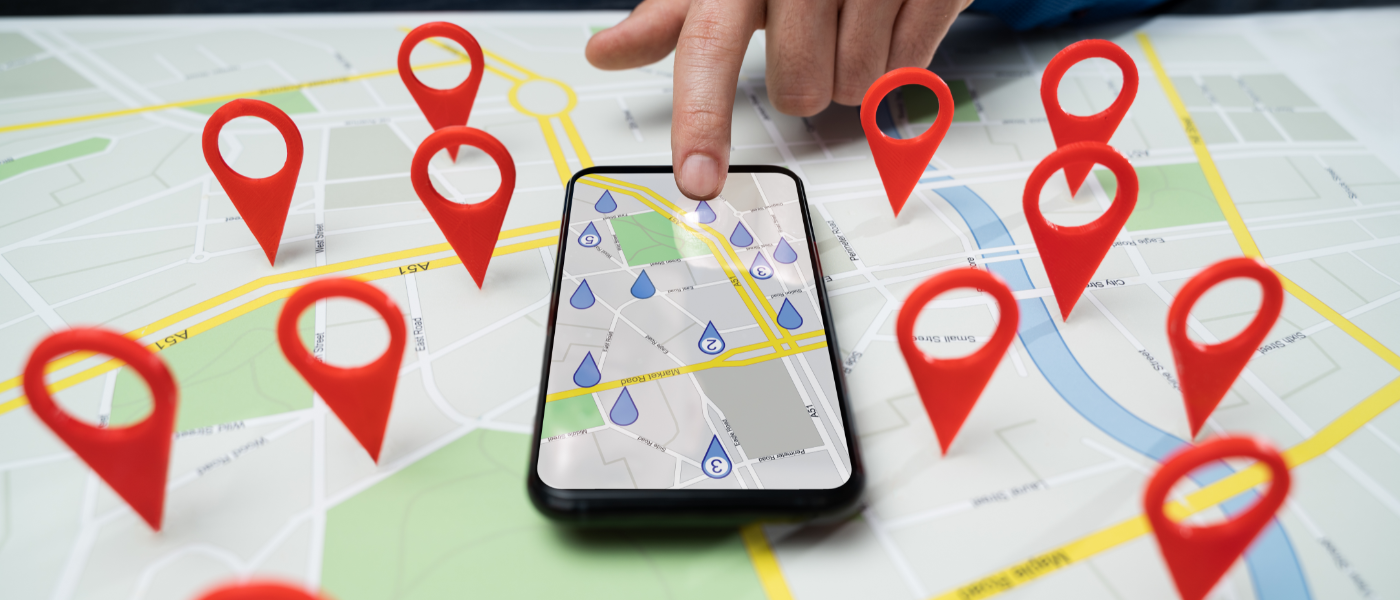 A photo of a smartphone laying on a map with several pin drops on the map. 